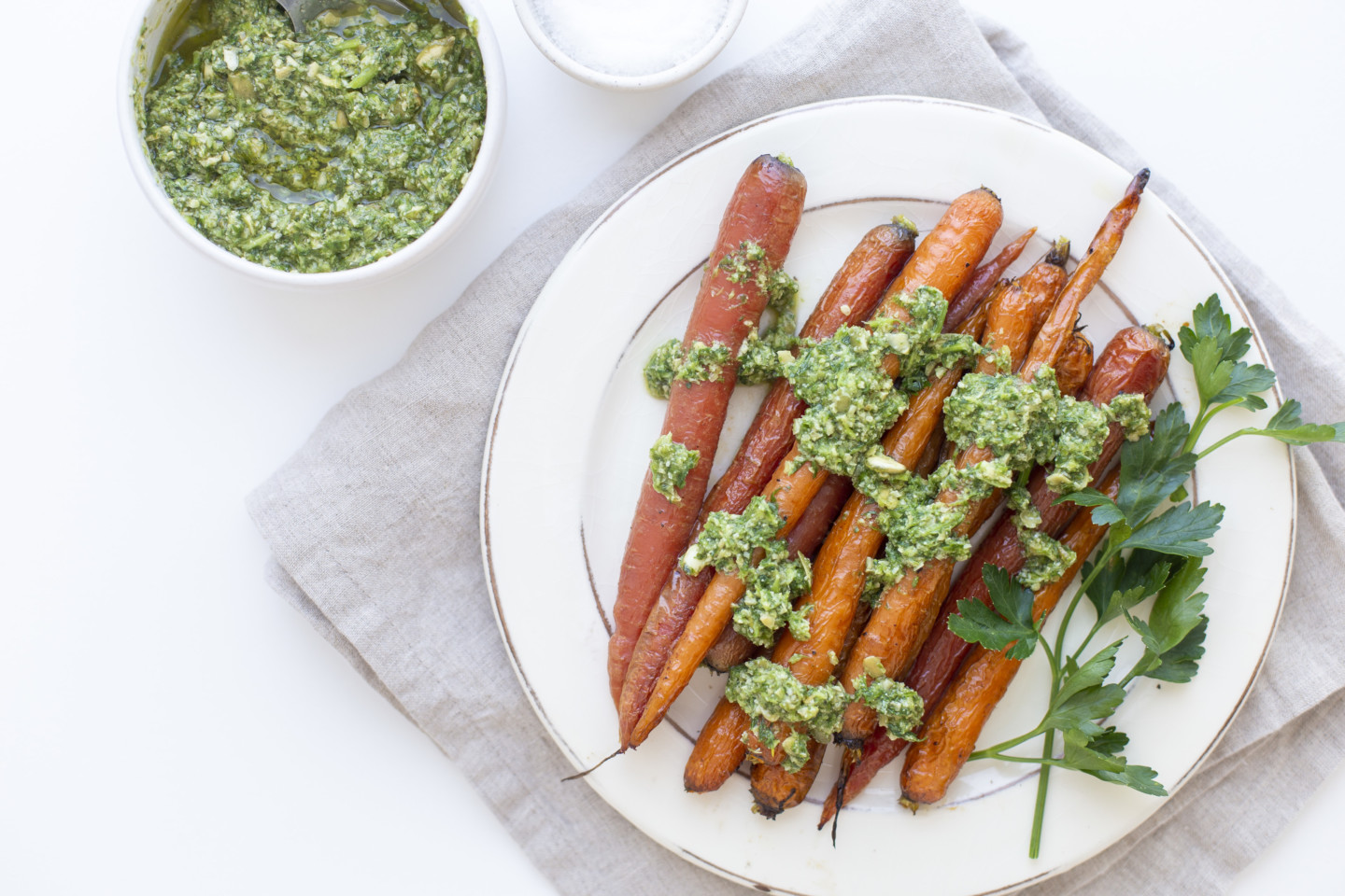 A plate of roasted carrots that are topped with carrot top pesto along with a smaller bowl of pesto.