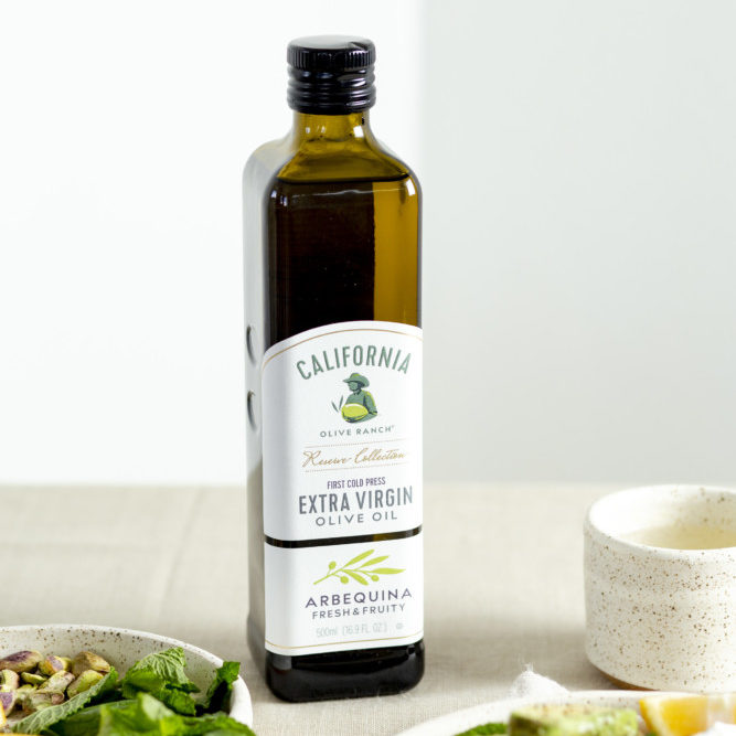 A bottle of California Olive Ranch Arbequina Extra Virgin Olive Oil sitting next to a dish of spring Panzanella salad.